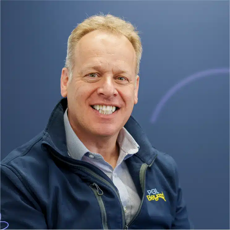 Person smiling, wearing a blue jacket over a collared shirt, standing in front of a blue background.