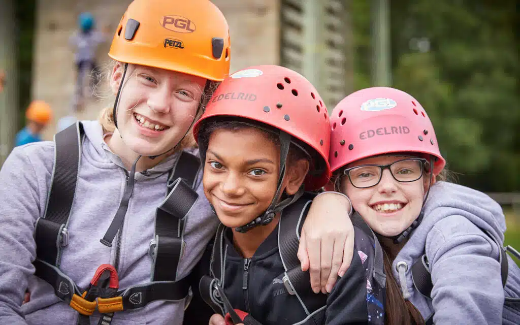 Three people wearing helmets and harnesses smile at the camera during an outdoor adventure activity.