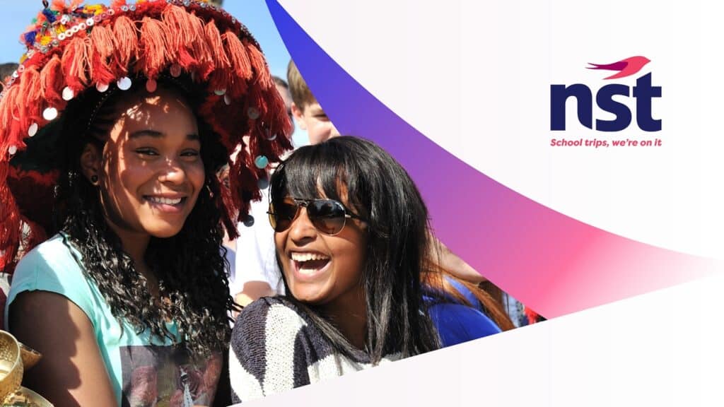 Two smiling girls, one wearing a colorful hat, stand outdoors with others in the background. NST logo and slogan "School trips, we're on it" are visible on the right.