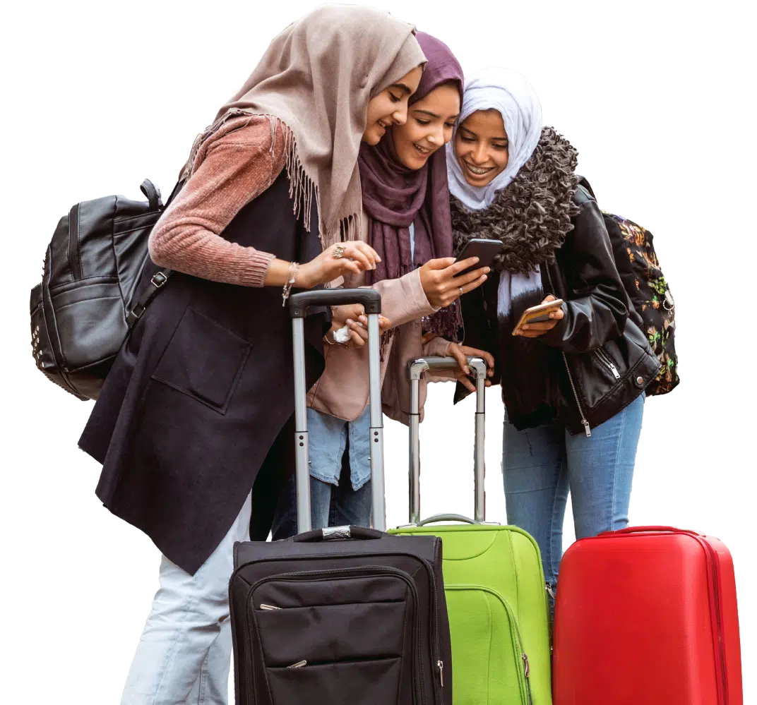 Three women with hijabs smile while looking at a smartphone, standing with backpacks and three suitcases, appearing ready for travel.