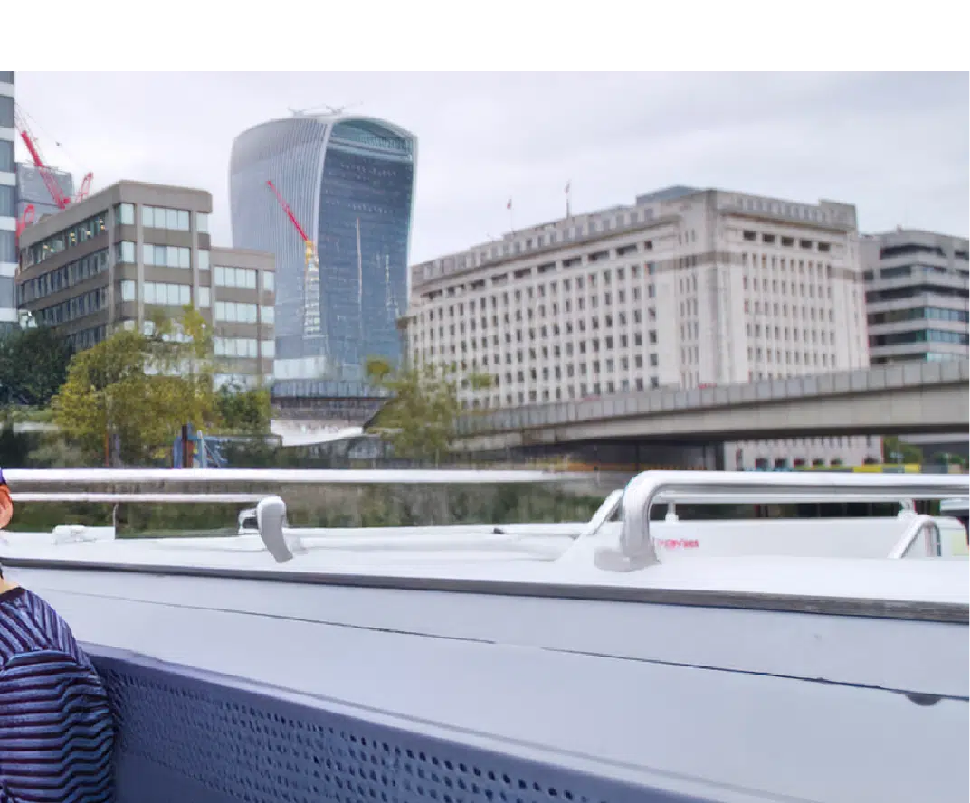 View of London buildings, including the Walkie Talkie skyscraper, seen from a boat on the River Thames with part of a passenger in the foreground.