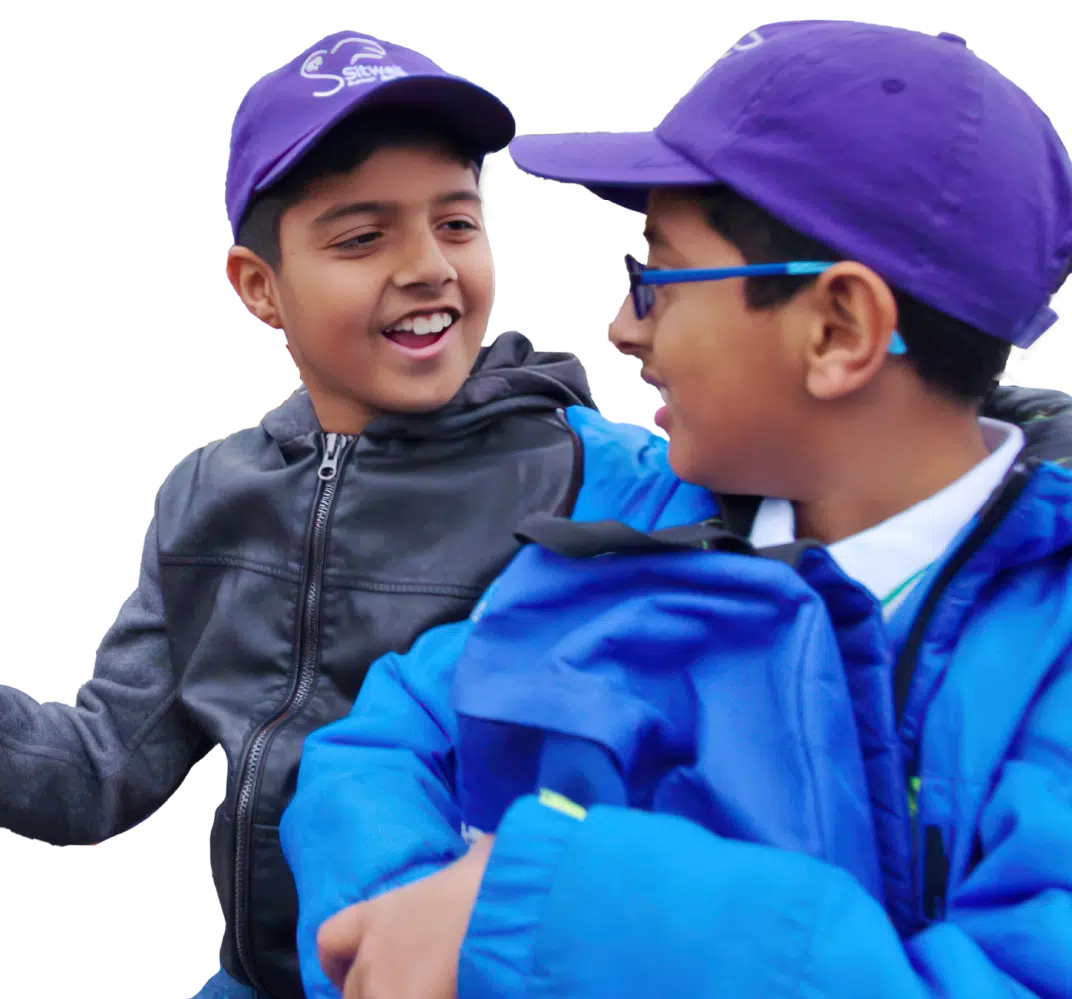 Two boys wearing purple caps and jackets smiling and talking to each other against a white background.