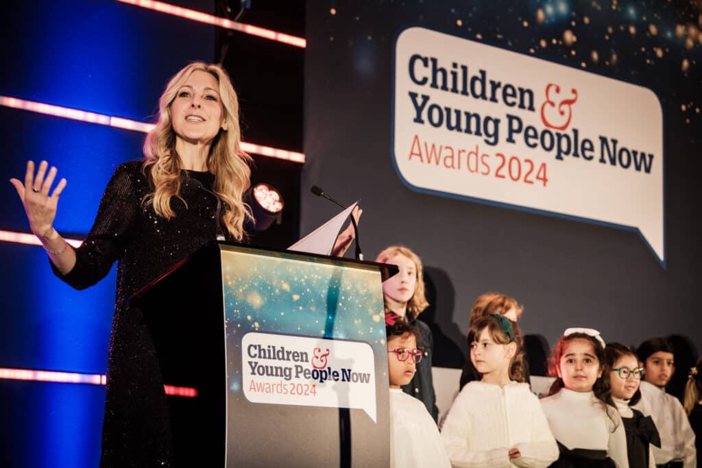 A woman speaks at a podium labeled "Children & Young People Now Awards 2024," with several children standing on stage beside her.