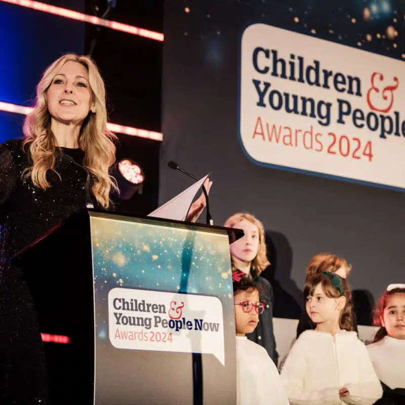 A woman speaks at a podium labeled "Children & Young People Now Awards 2024," with several children standing on stage beside her.