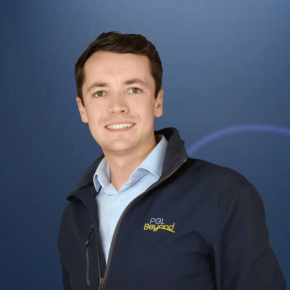 A man with short brown hair wearing a light blue shirt and a navy jacket with the "PGL Beyond" logo poses in front of a blue background.